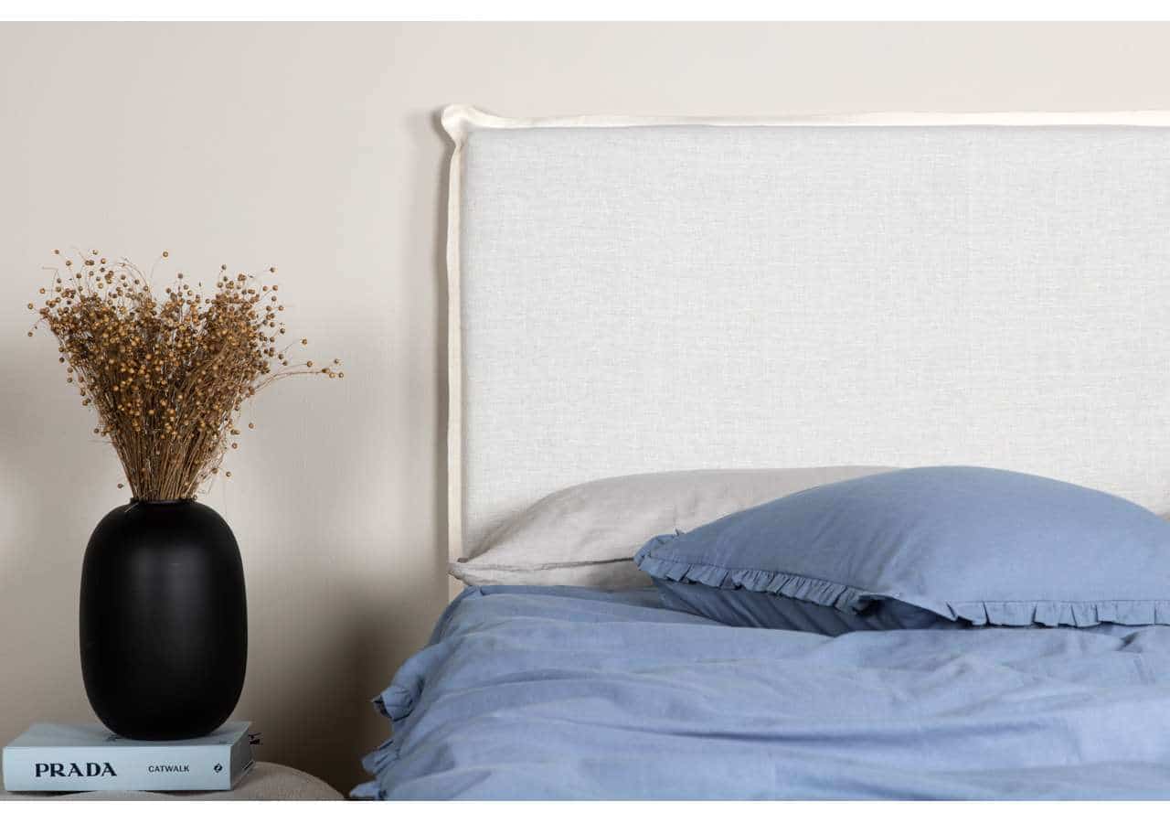 Ljust sovrum med blå sängkläder och vita väggar samt en dekorativ svart vas på nattduksbordet.