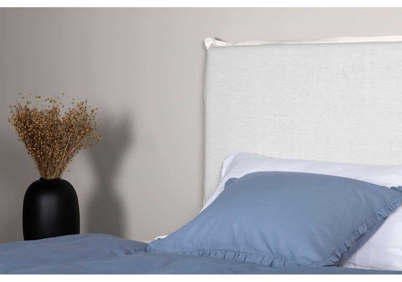 Lågupplöst säng med blåa örngott och vita sängkläder framför en vit sänggavel.