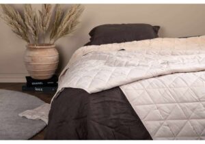 Mjuk bomullssäng med svart täcke och dekorativ blomsterkruka i sovrum.