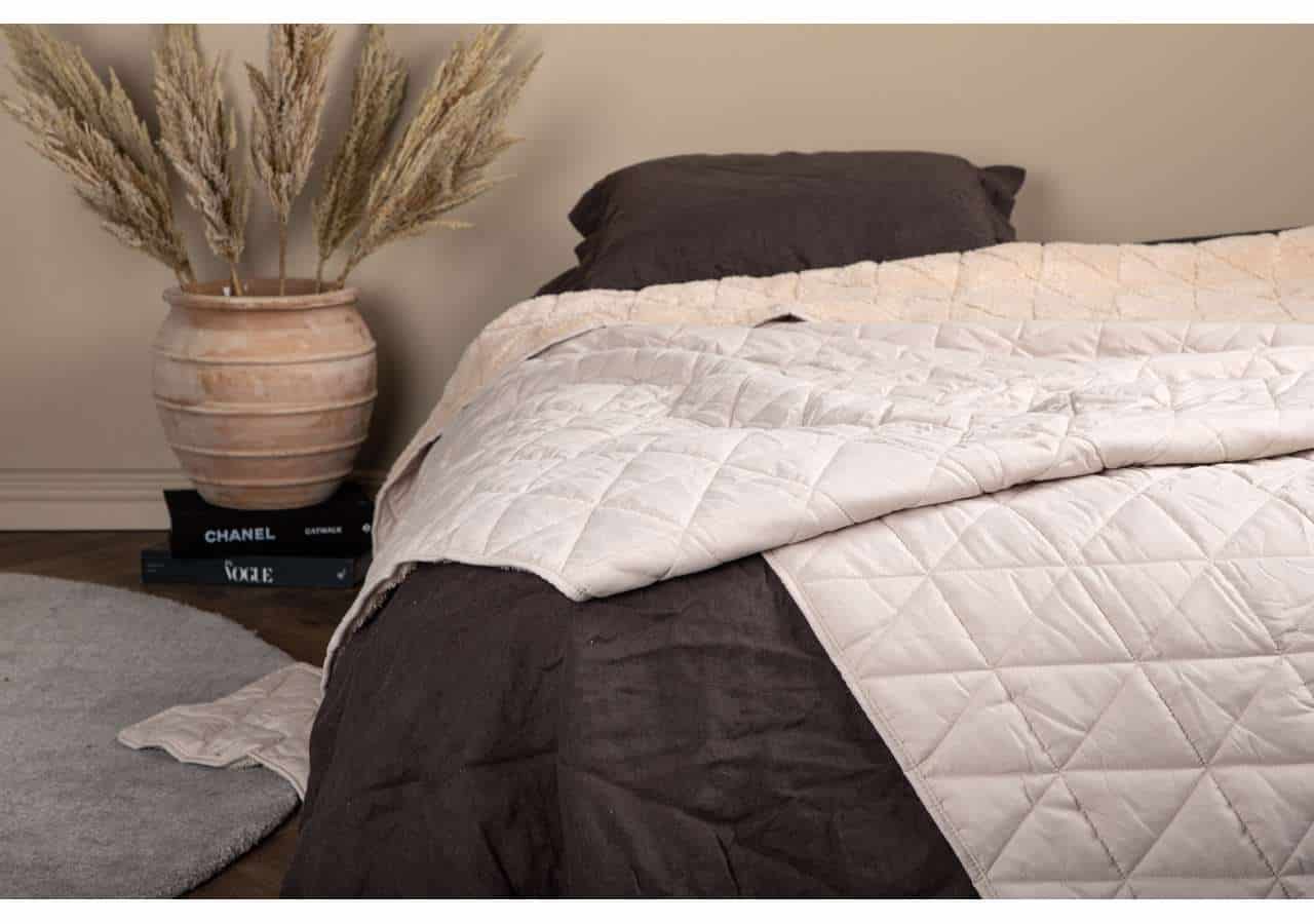 Mjuk bomullssäng med svart täcke och dekorativ blomsterkruka i sovrum.