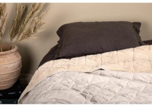 Långpåsäng med mörkbrunt örngott och vit bäddmadrass på slitet trämöbler.