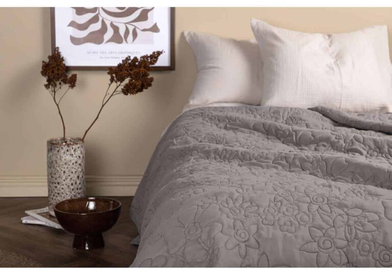 Ljust sängklädesset med quiltad överkast och vita örngott i elegant sovrumsmiljö.