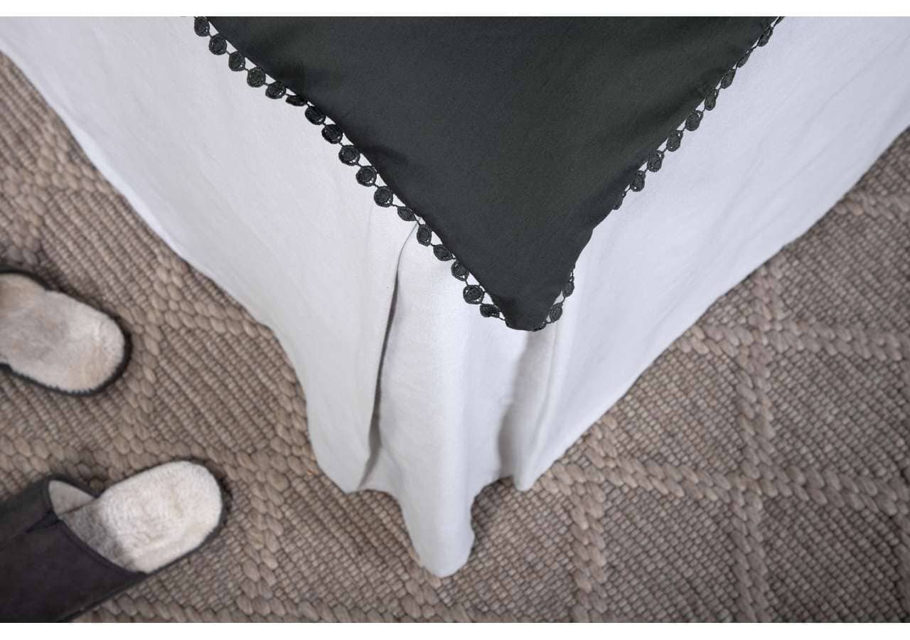 Mjukt sängöverkast med svart kant och pompomband, elegant design för sovrum.