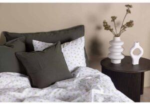 Mörkgråa sängkläder och kuddar med vit och gul blomsterprint på säng.