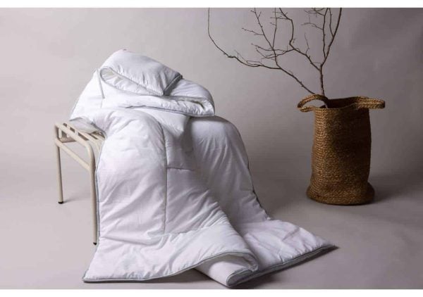 Liggandes täcke och kuddar i vit sängtextil, stilren och bekväm sovmiljö.