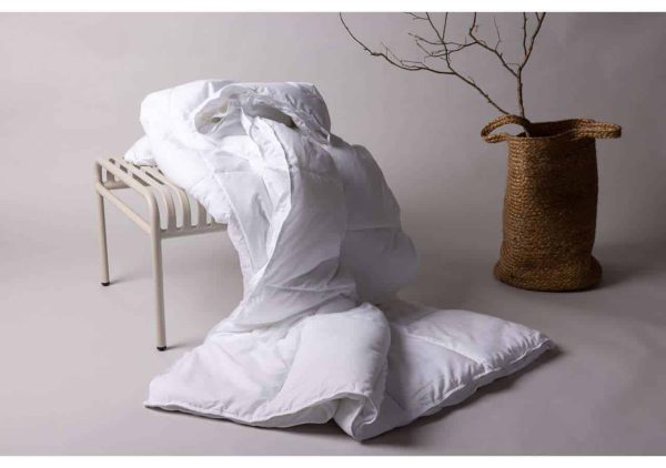 Lakan och sängkläder i vitt på golvet med en liten sits och en växt i korg.