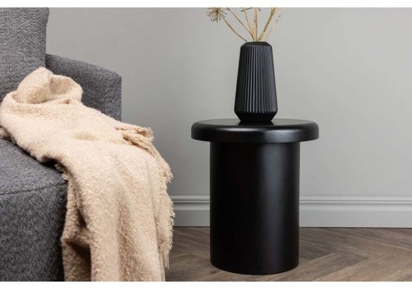 Skrivbordslampa i svart med dekorativ vas, nära bekvämt soffbord och filt.