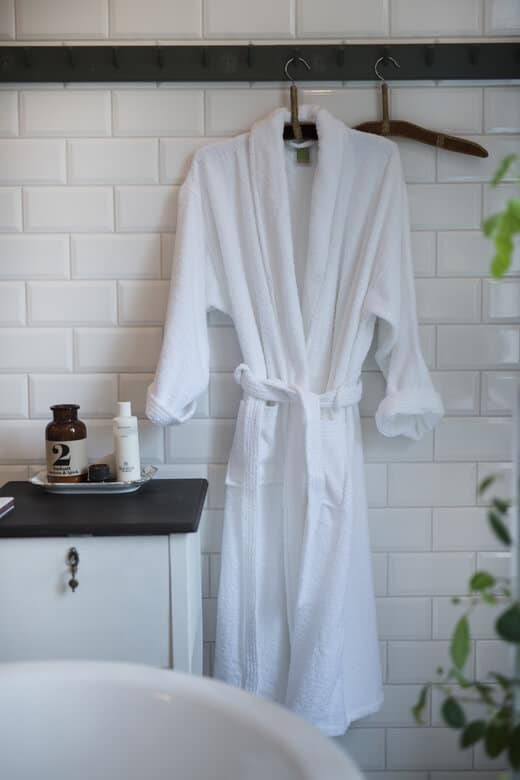 Ljus vit morgonrock av bomull på badrumsvägg med moderna hotellstil detaljer.