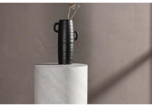 Mörk vas med handtag på marmorpodium, minimalistisk inredning.