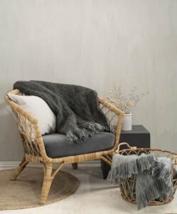 Ljus soffstol i rotting med gråa textilier och växtdetalj i vit vas.