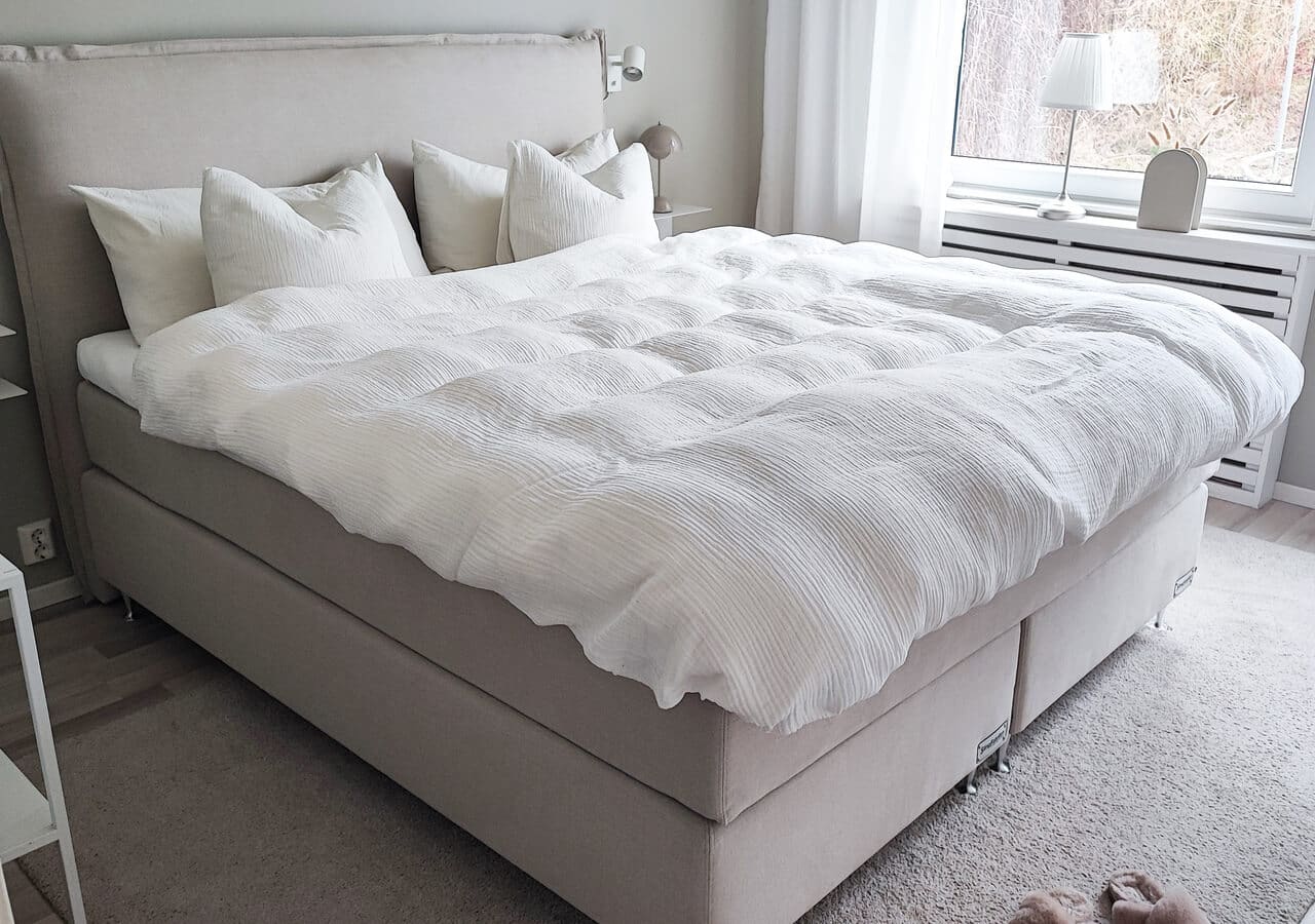 Långsömnad säng med vit sängkläder och kuddar i ett sovrum.