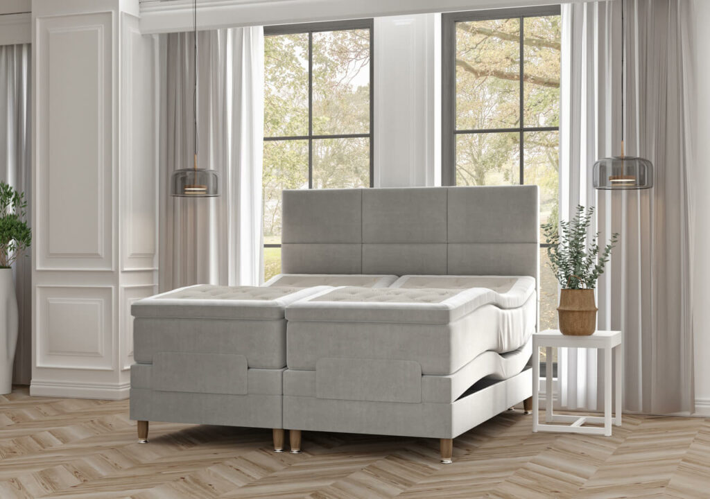 Liggande säng med modulärt madrassystem i ljusgrått tyg i ett välkomnande sovrum.