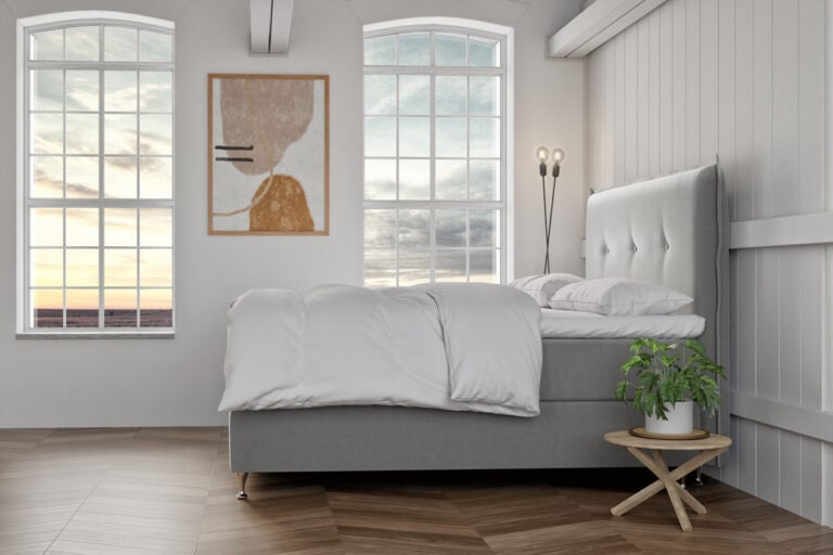 Ljust sovrum med stor säng och vita sängkläder, modern inredning och stora fönster.