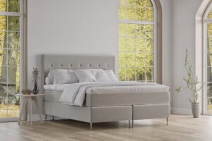 Elegant säng från Sängfabriken i modern design med vita textilier och stora fönster.
