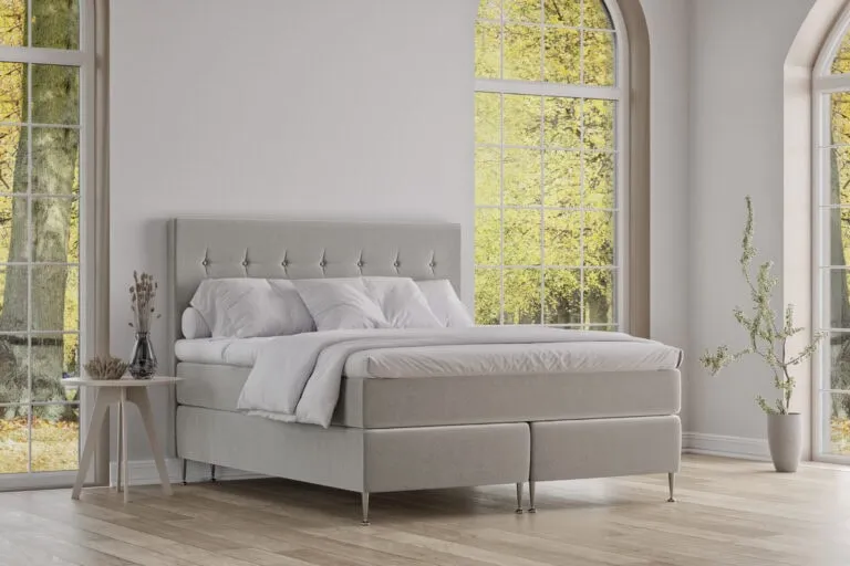 Elegant säng från Sängfabriken i modern design med vita textilier och stora fönster.