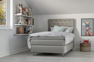 Madrass och sängram i modern sovrumsmiljö med leksaker och barnsäng.