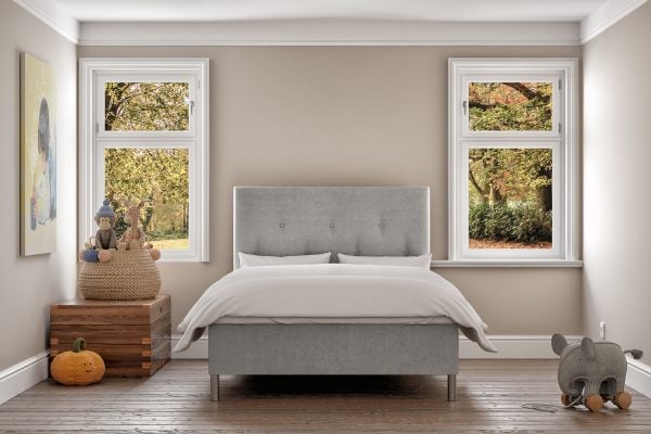 Ljust sovrum med sängfabriken-säng, stora fönster och mysiga dekorativa detaljer.