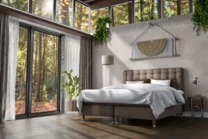 Ljust sovrum med stora fönster mot natur, modern säng och gröna växter, perfekt för avkoppling.