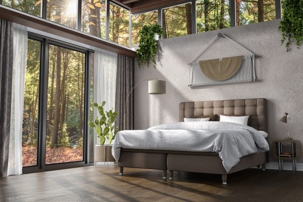 Ljust sovrum med stora fönster mot natur, modern säng och gröna växter, perfekt för avkoppling.