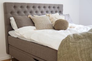 Mordern säng med grått huvudgavel och dekorativa kuddar, perfekt för sovrum inredning.