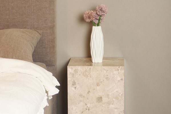 Ljus säng och nattduksbord i marmor med blomsterarrangemang, modern inredning.