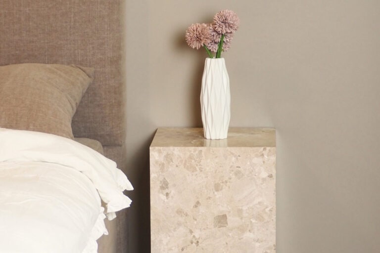 Ljus säng och nattduksbord i marmor med blomsterarrangemang, modern inredning.