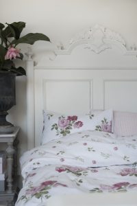 Mönstrad sängkläder med blommor, sänggavel i vitt trä, elegant sovrumsstil.