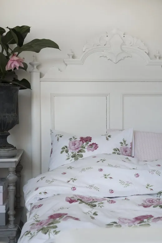 Mönstrad sängkläder med blommor, sänggavel i vitt trä, elegant sovrumsstil.