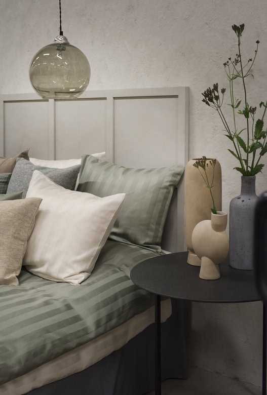 Ljust sovrum med stilrena sängkläder och moderna vaser för ett avkopplande hem.