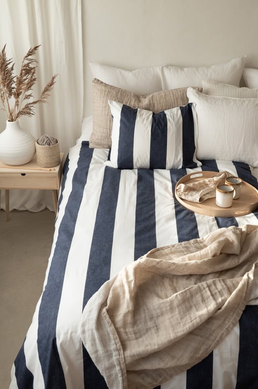 Ljus och stilren säng med blåvita randiga sängkläder och fluffiga kuddar.