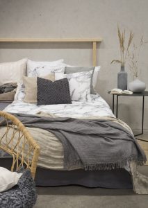 Mjukt bäddset i marmerprint med kuddar och pläd, skapar en elegant och inbjudande sovmiljö.