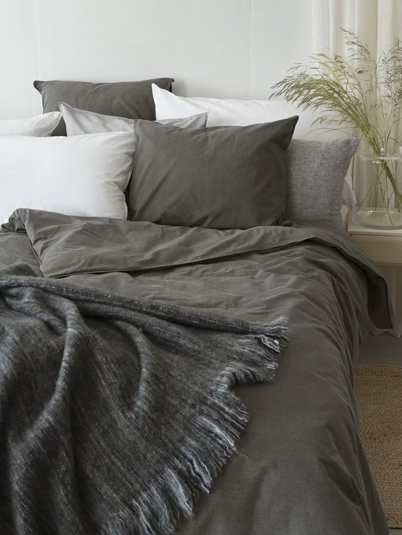 Mörkgrå sängkläder och kuddar i mysigt sovrum med växtdetalj.