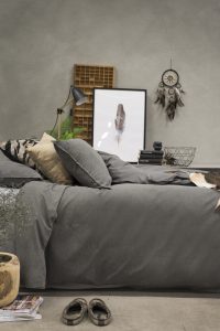 Mjuk säng i grå nyanser med dekorativa kuddar och moderna posters.