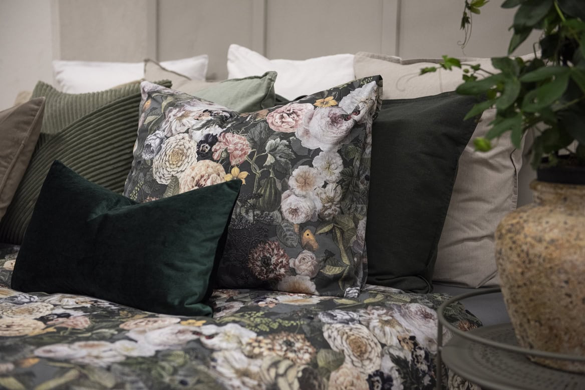 Blommönstrade och mörka sängkläder i säng med många kuddar för ett elegant sovrum.