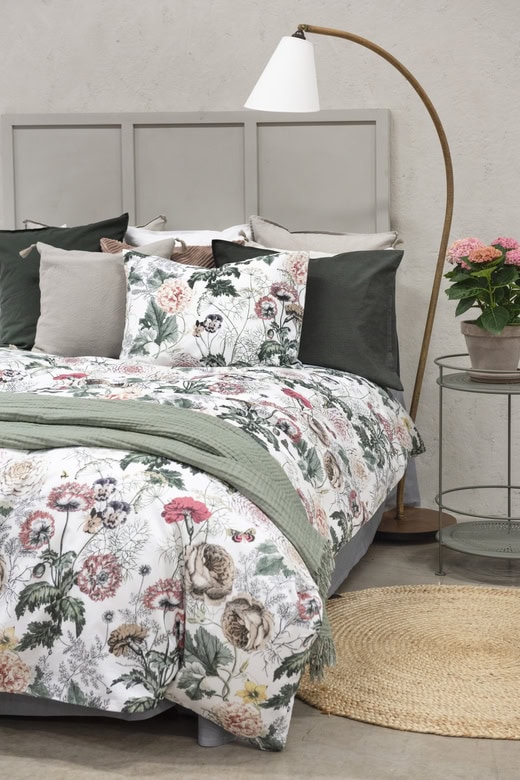 Mjuka sängkläder och prydnadskuddar i blomsterprint för en mysig sovrumsatmosfär.