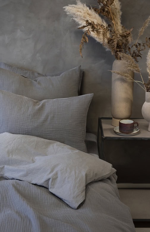 Ljust sovrum med sängkläder i mjukt grått och beige, modern inredning med pampiga växter.