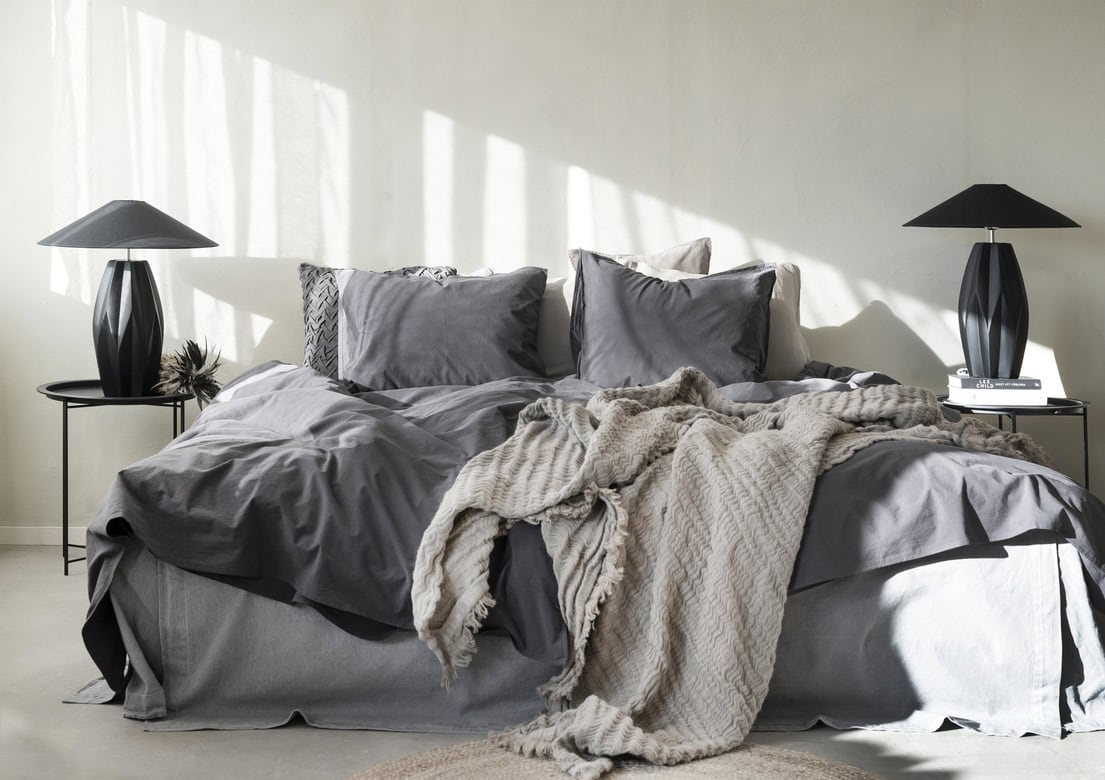 Mörkgrå sovrumsinredning med sängkläder och ljusstakar, modern och stilren design.