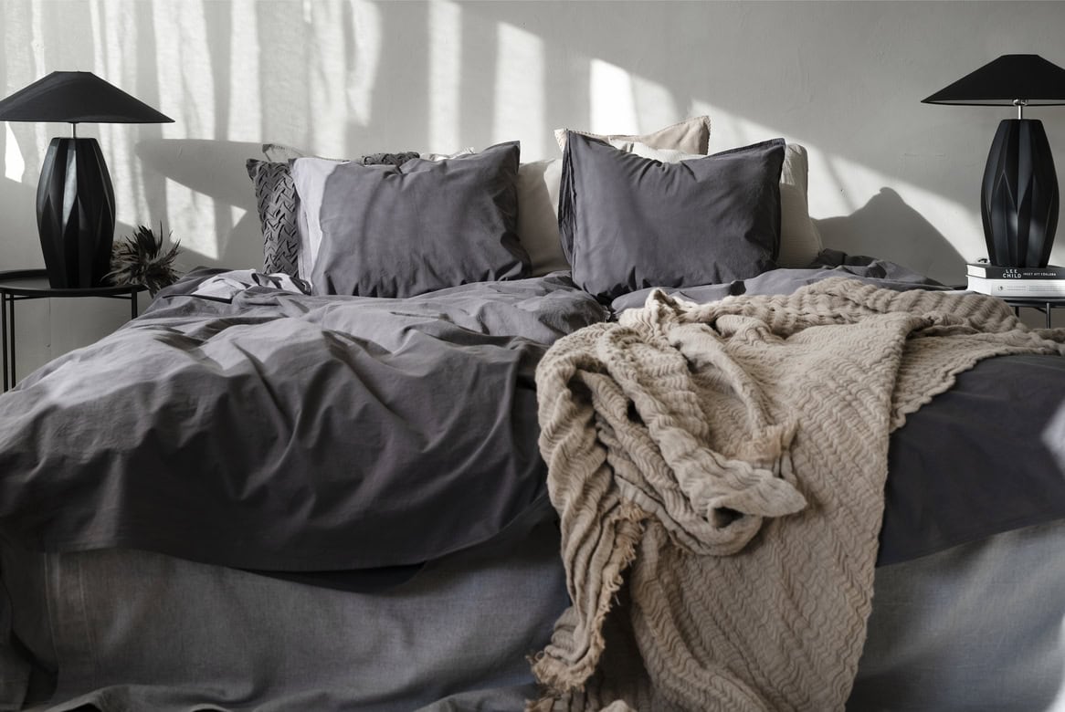 Mörkgrå sängkläder med mysig beige filt på sängram i sovrum.