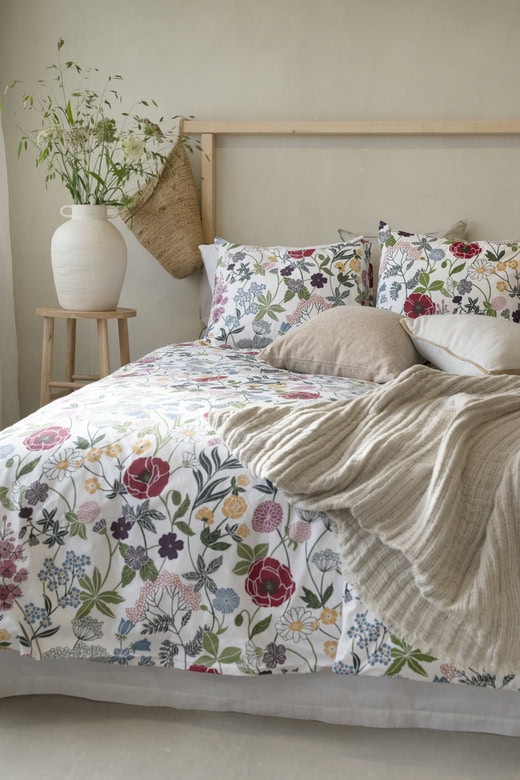 Ljust sovrum med blomsterdraperi och naturliga textilier, perfekt för en tjejmiddag och mysig sömn.