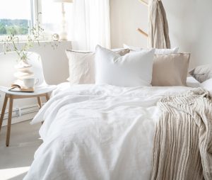 Ljust sovrum med sängtäcke och kuddar i vit och beige toner för en lugn miljö.