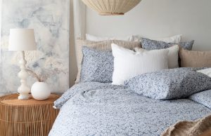 Avslappnad sovrumsmiljö med sängkläder i blå och vita nyanser, mysig belysning och naturmaterial.