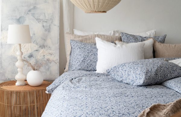 Avslappnad sovrumsmiljö med sängkläder i blå och vita nyanser, mysig belysning och naturmaterial.