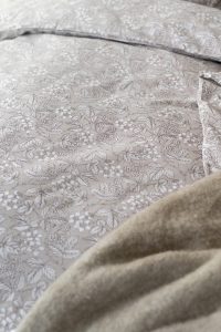 Lakan med blomster- och bladmotiv i mjukt beige och vitt, elegant sovrumsaccessoar.