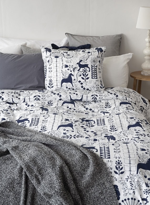 Mysigt sovrum med blå och vit sängkläder, dekorativa kuddar och skandinavisk stil.