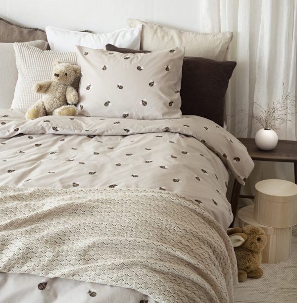 Mjuka sängkläder med getingmönster och mysiga prydnadskuddar i naturnära färger.
