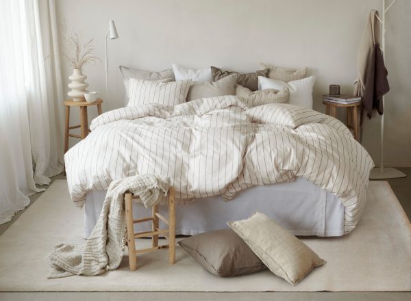 Mjuk säng med naturnära sängkläder och många kuddar, skapar ett inbjudande sovrum.