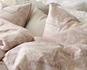 1. Mjukt sängöverkast och matchande örngmålen i puderrosa och beige med elegant mönster.