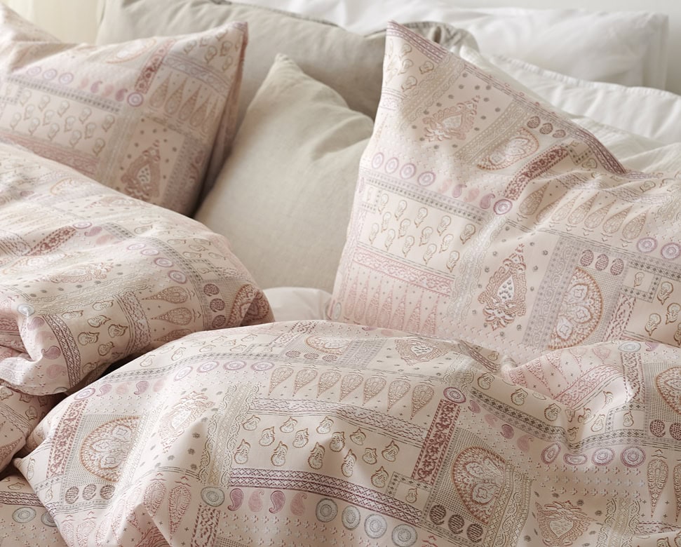 1. Mjukt sängöverkast och matchande örngmålen i puderrosa och beige med elegant mönster.