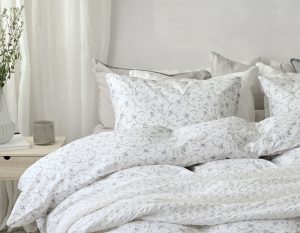 Linneduk med blomsterprint i vit och ljusgrå, stilrent bäddarrangemang.