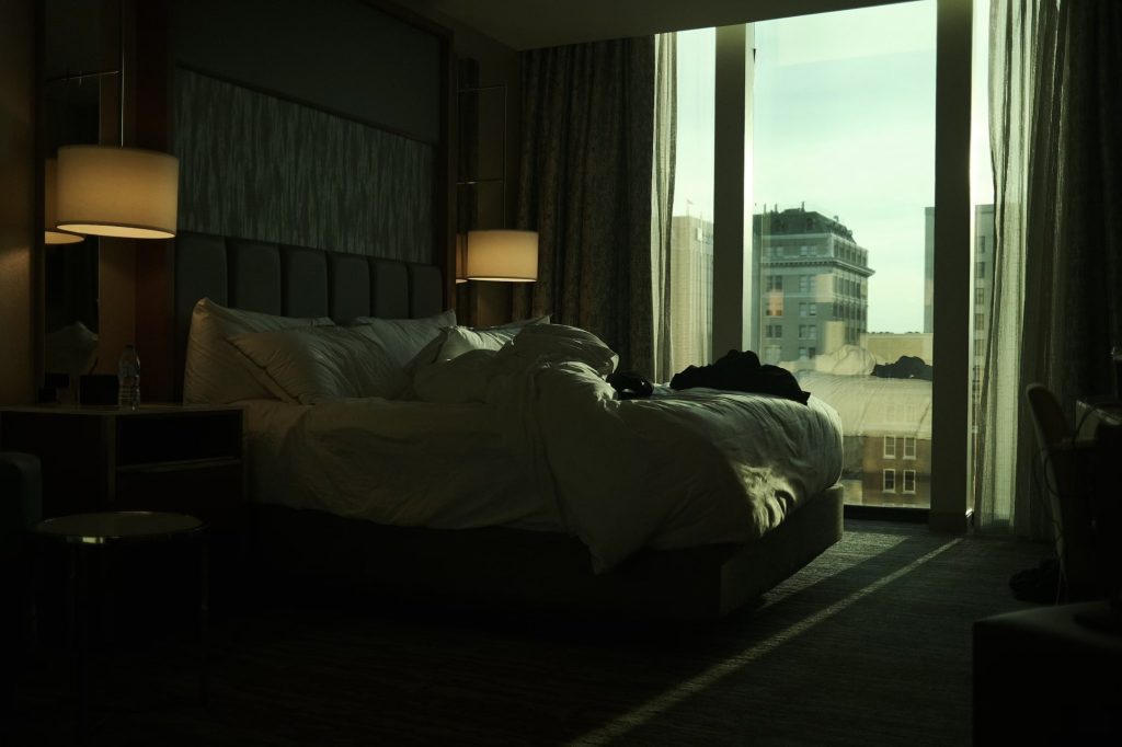 Ljus sovrumsbild med säng och stor fönsterutsikt över staden, inbjudande och stilrent.